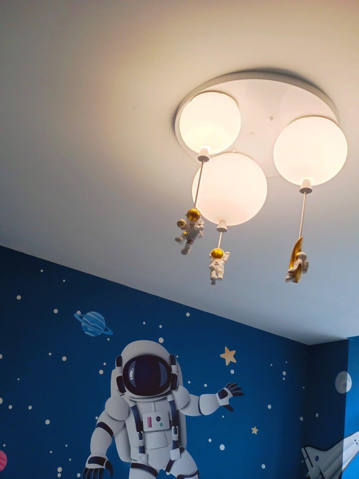 Three pale balloon shades lit above a space mural