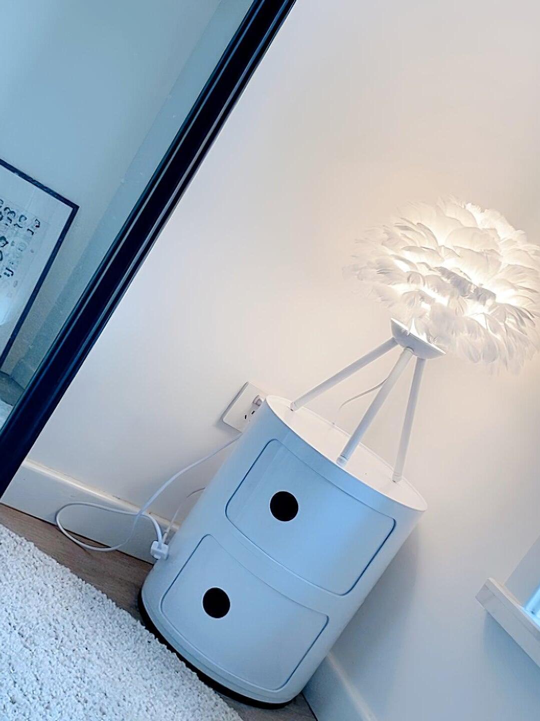 White tripod lamp angled on small drawer unit
