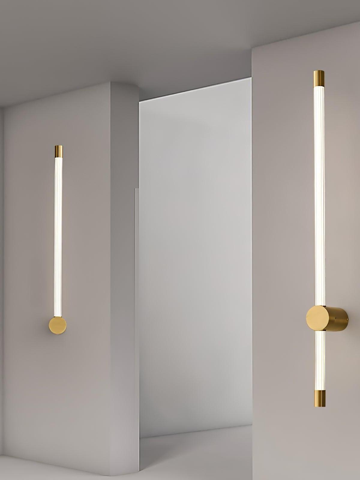 Two brass-tone tube wall lights beside a doorway, one single tube and one with long and short sections