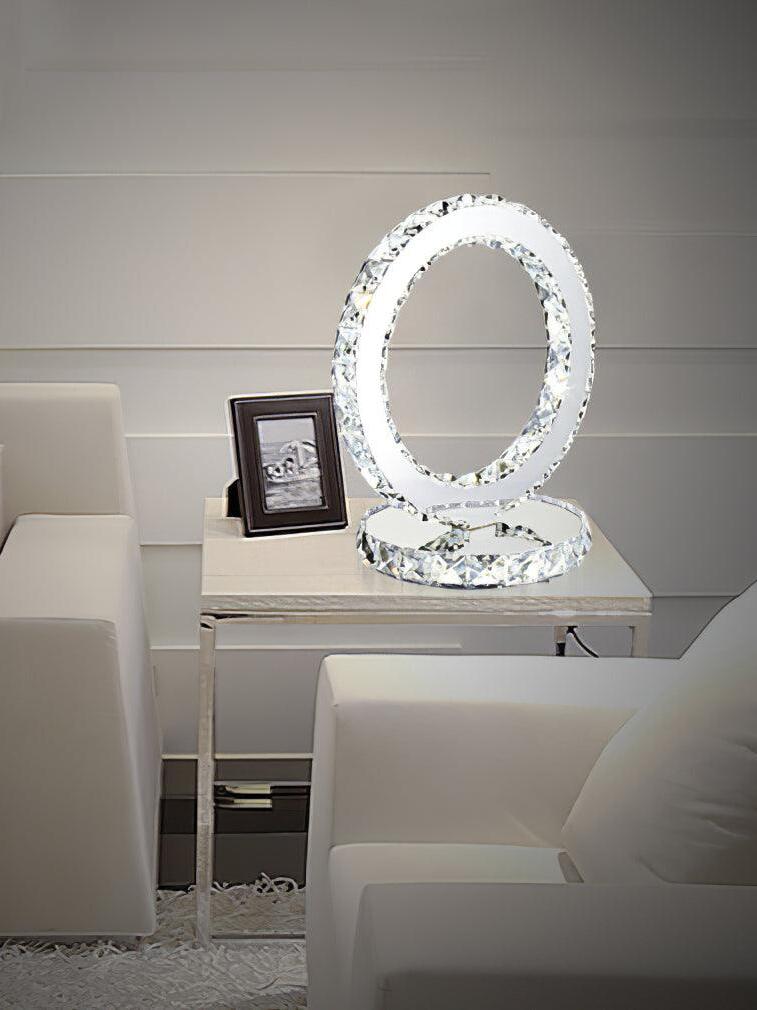 Illuminated ring lamp on a white bedside table with a framed picture beside a bed