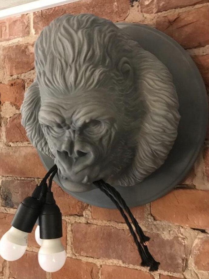 Grey gorilla relief on red brick wall with dark holders and white round bulbs