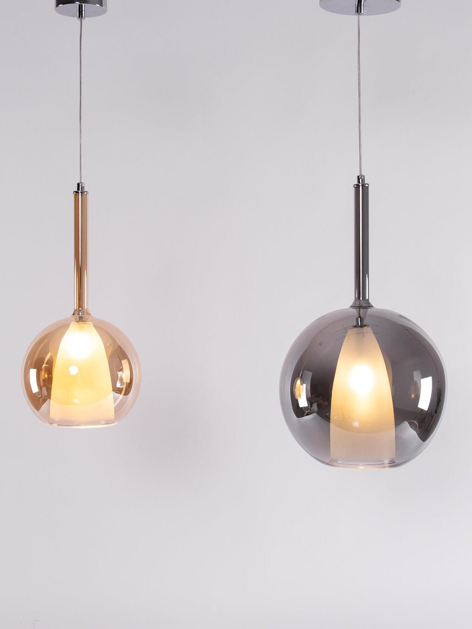 Two separate globe pendants in amber-looking and dark reflective finishes below round canopies
