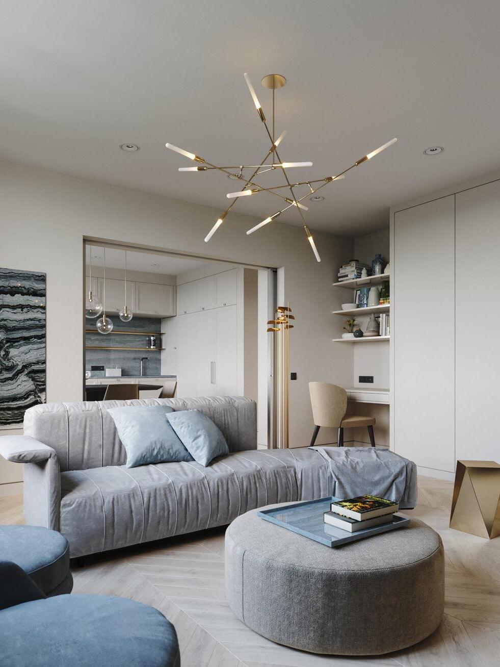 Gold-coloured branching chandelier above a grey sectional sofa and round ottoman