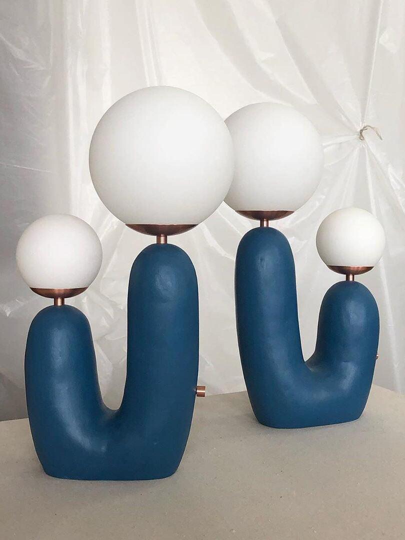 Two blue Oo Rough twin-globe lamps facing opposite ways before a white backdrop, with side control visible