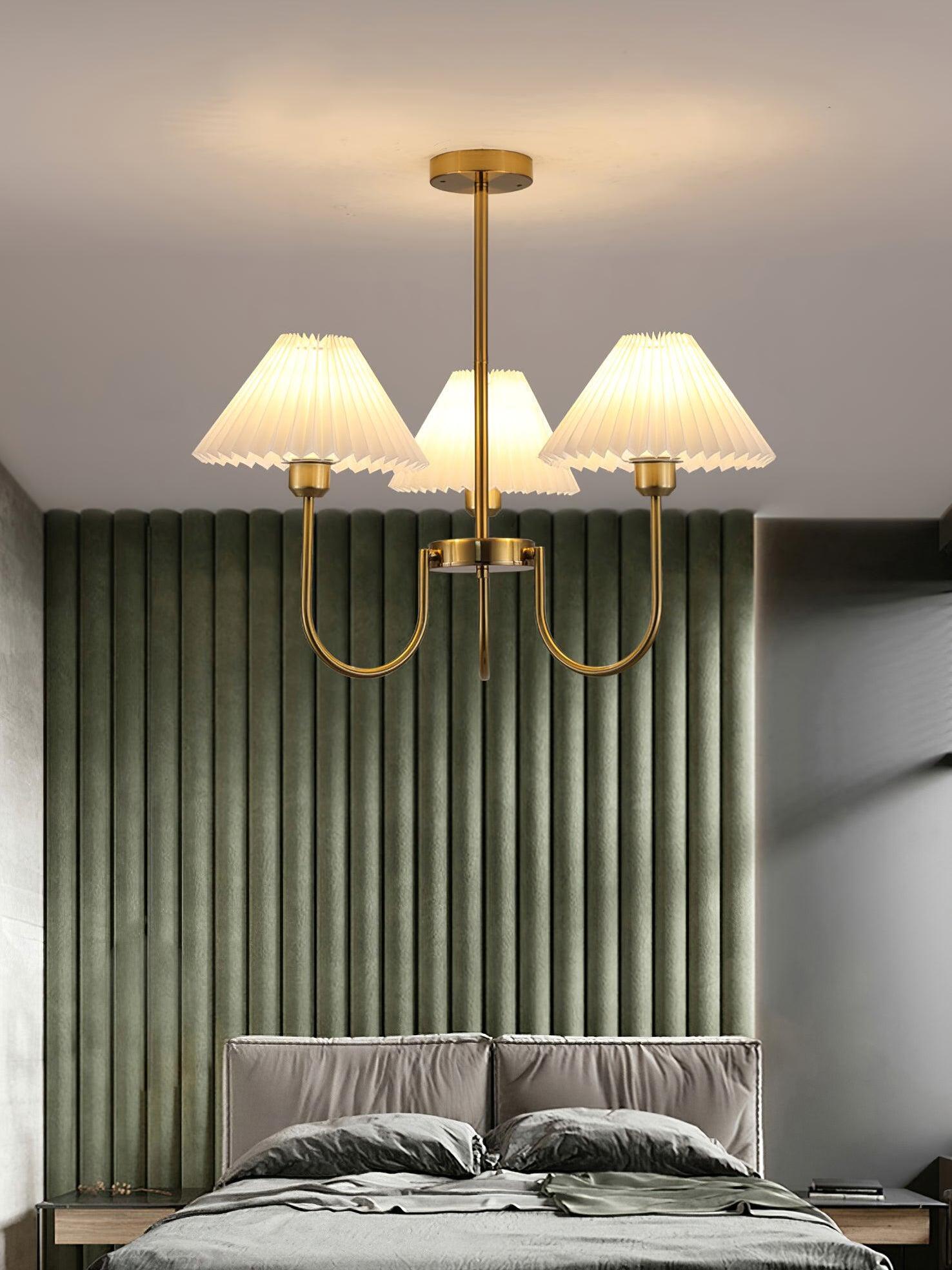 Lit three-shade chandelier above a bed in front of a vertically textured green wall