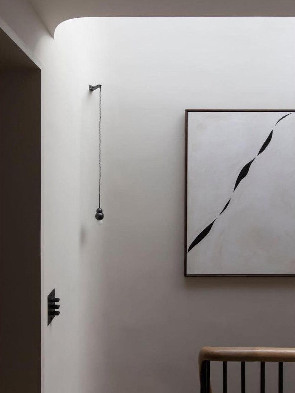 Black wall bracket with long suspended bulb near framed print
