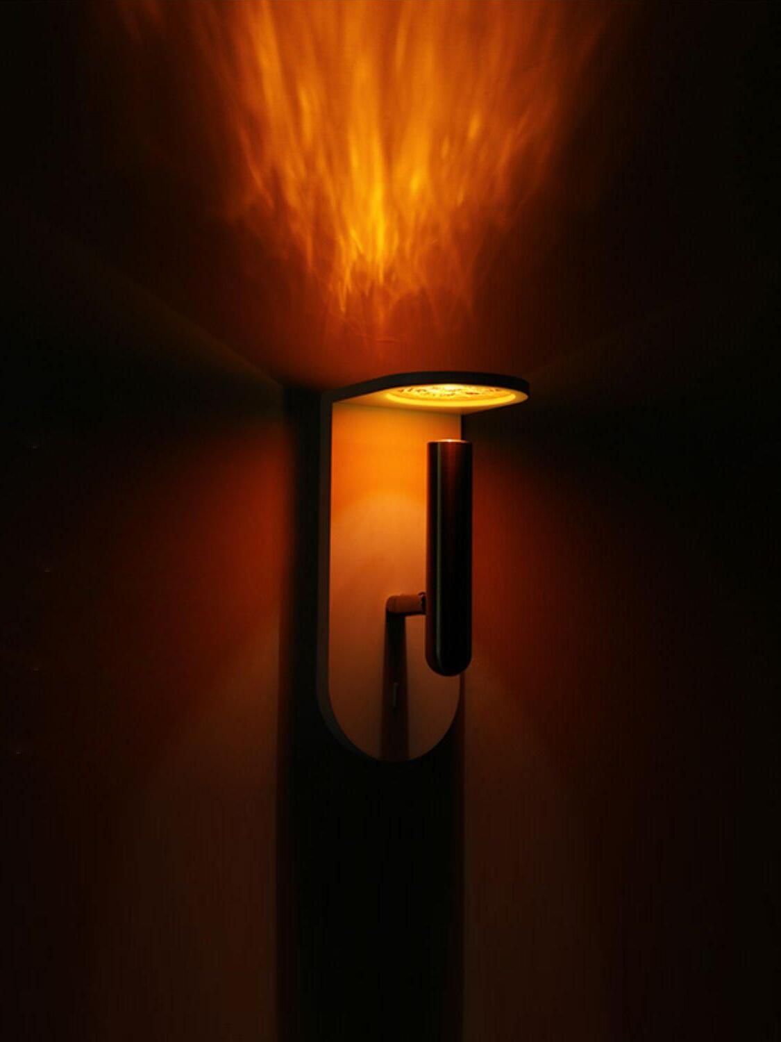 Black Nights wall light illuminated in a dark setting, with an orange pattern on the wall above