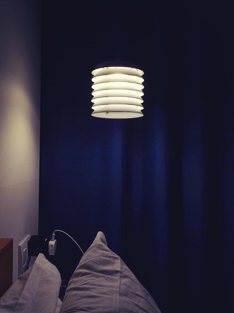 Glowing white stacked pendant beside bed against dark blue wall