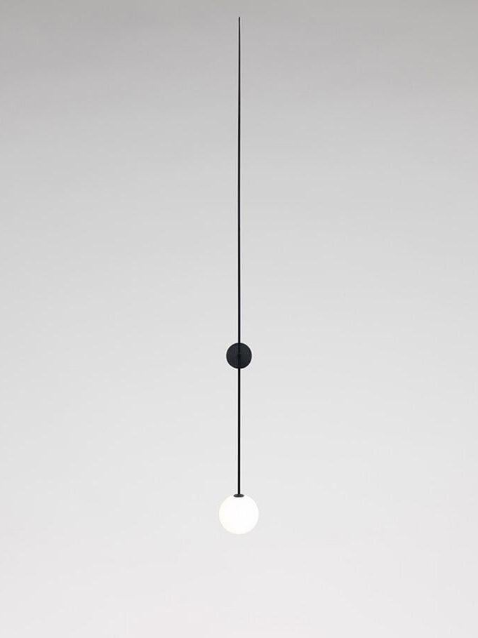Frontal black linear wall light with a glowing white globe and round backplate behind the rod