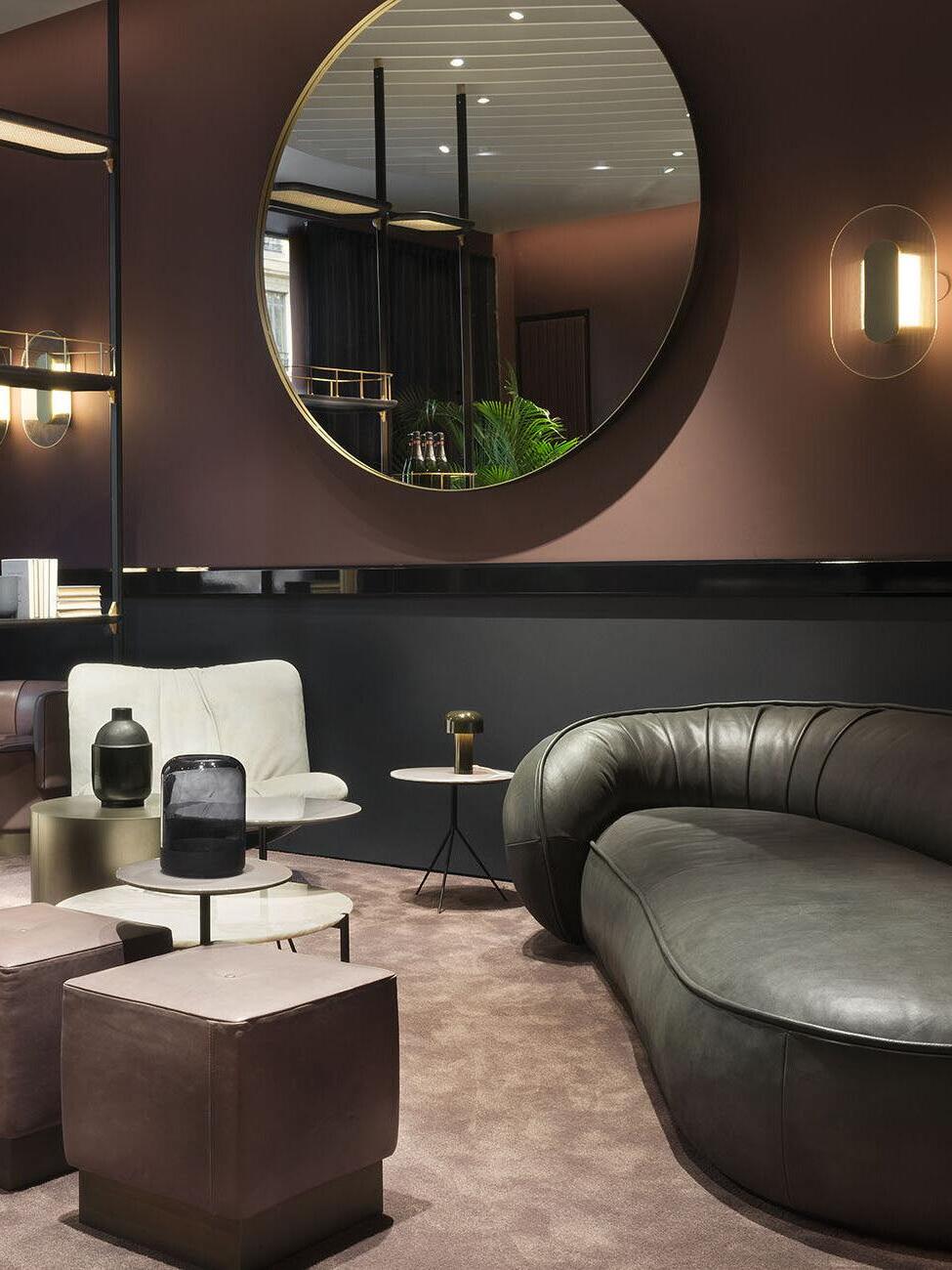Elongated Button wall light beside a large round mirror above dark lounge seating