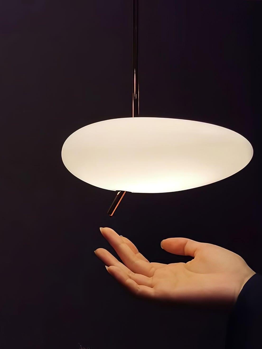 Close-up of a glowing white shade and rose-gold lower stem above an outstretched hand