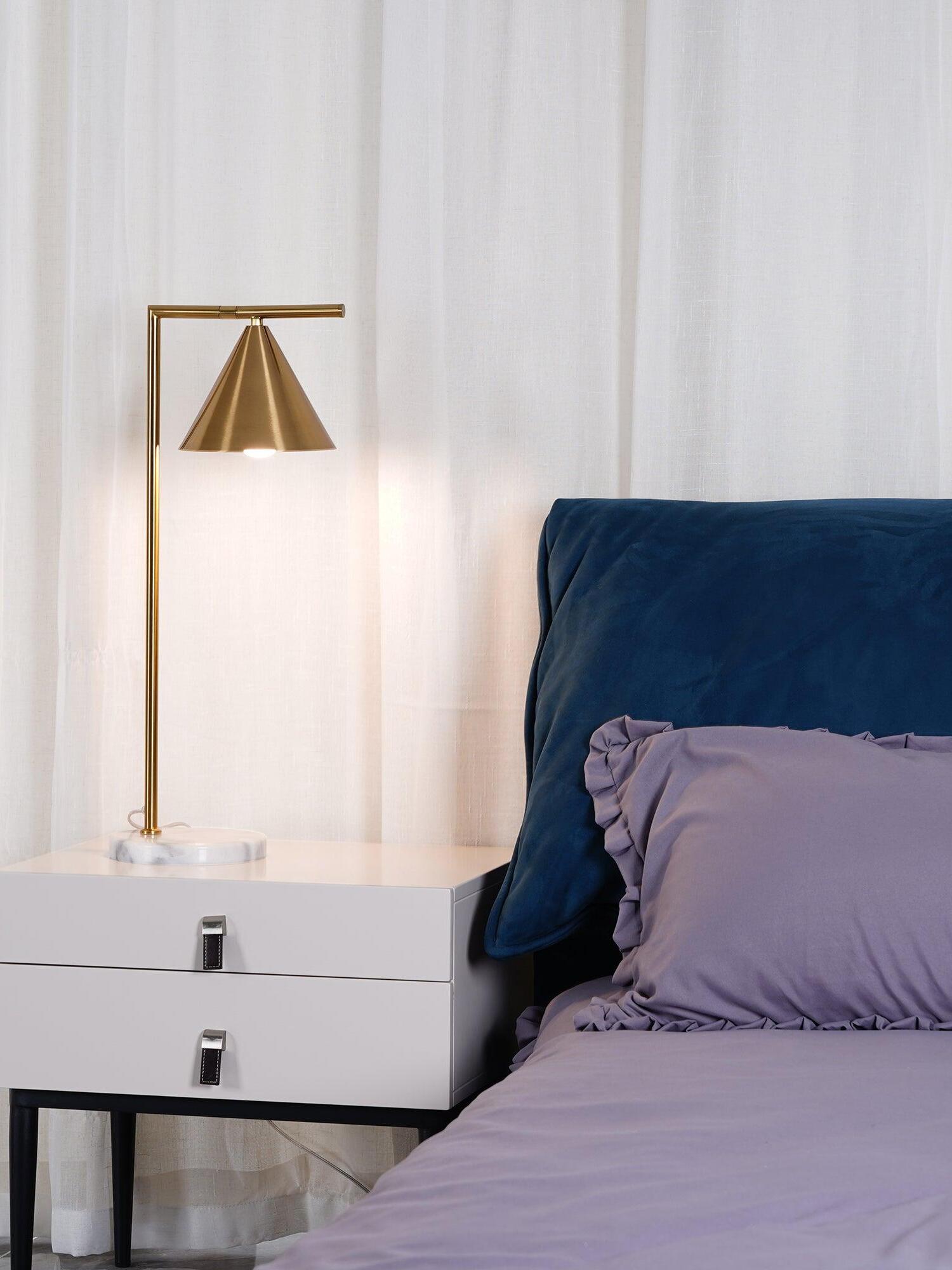 Downward-facing gold-tone cone lamp on white bedside cabinet