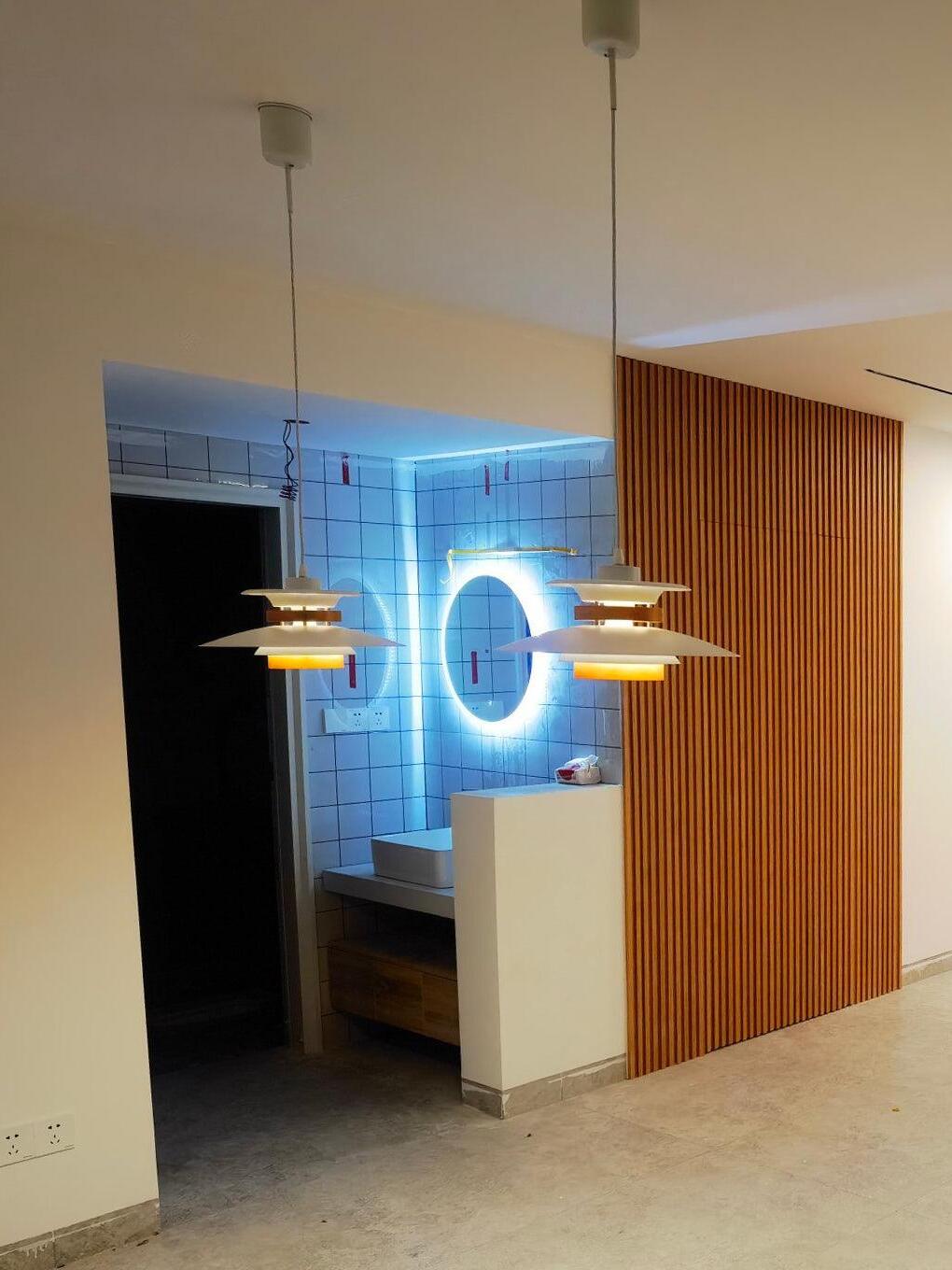 Two layered pendants near wood panelling and a round illuminated mirror