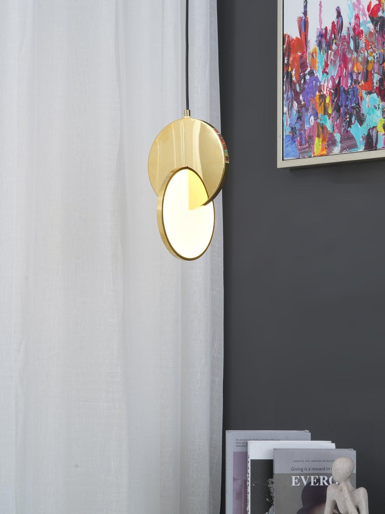 Lit gold disc pendant light beside white curtains, a dark wall and a colourful painting