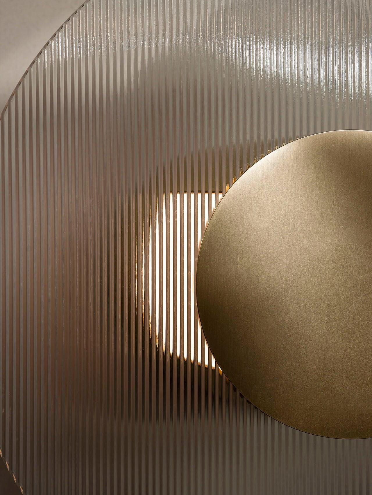 Close-up of vertical glass ribs, part of a gold-coloured round centre and light behind the glass