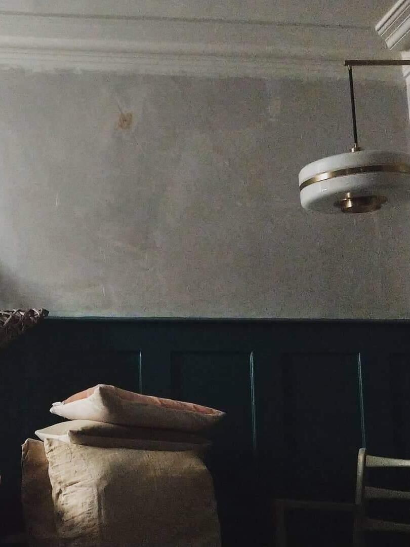 Unlit pale drum shade with metallic band in dim bench-and-cushion room