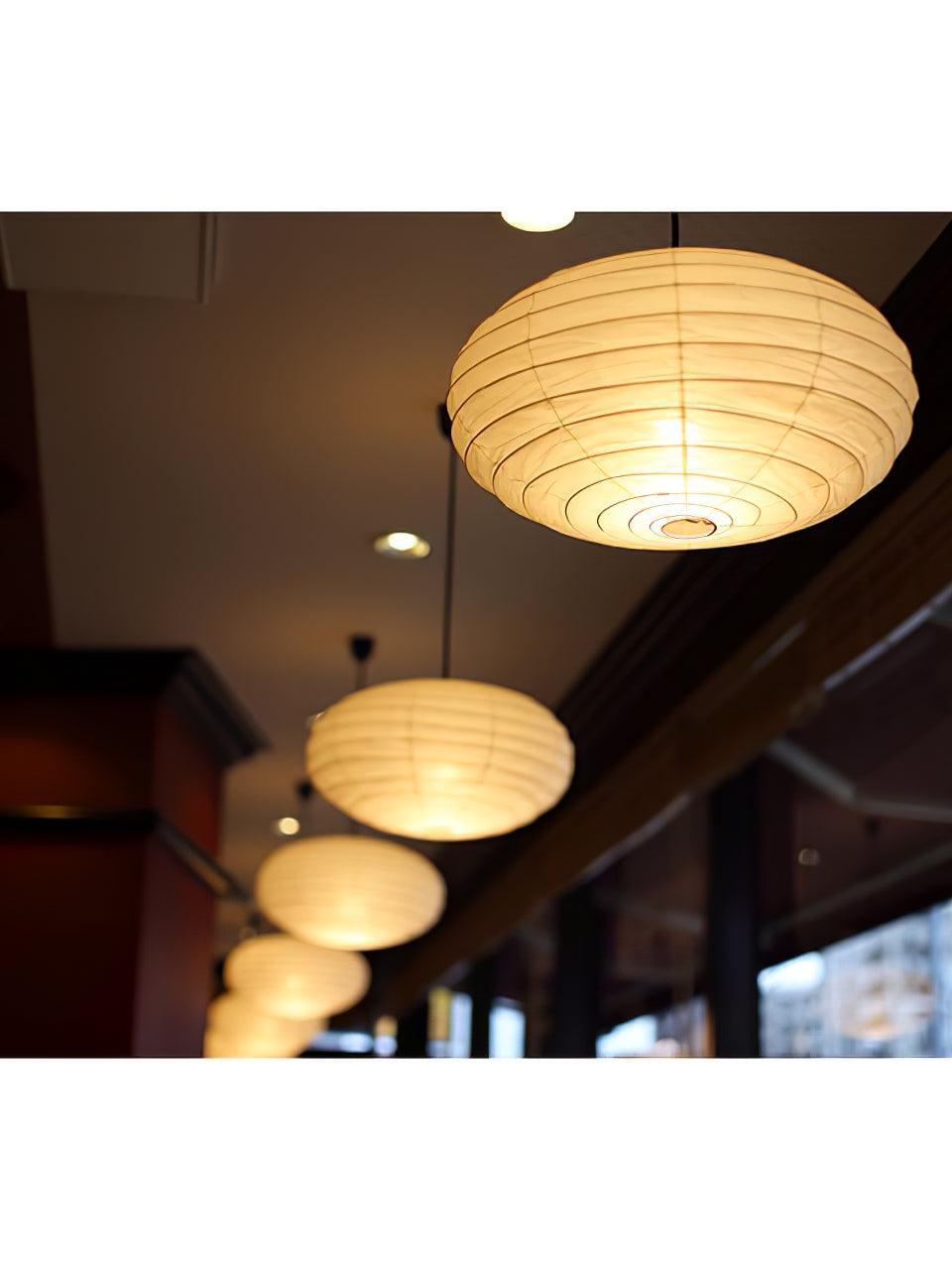 Row of glowing paper lanterns near windows, with concentric ribs and a small bottom opening visible on the front shade