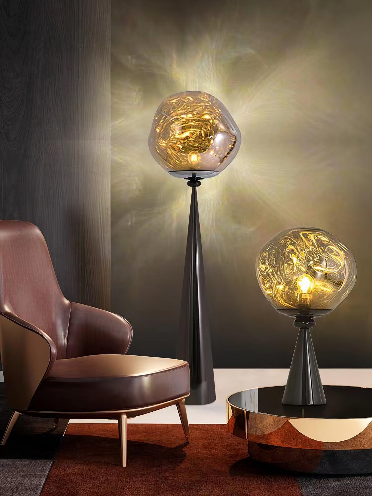 Black globe table lamp on a reflective coffee table beside a leather chair and a tall floor lamp