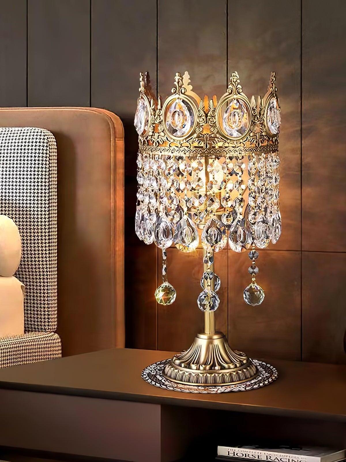 Crystal table lamp with long lower drops on a dark side table beside a chair and wooden wall panels.
