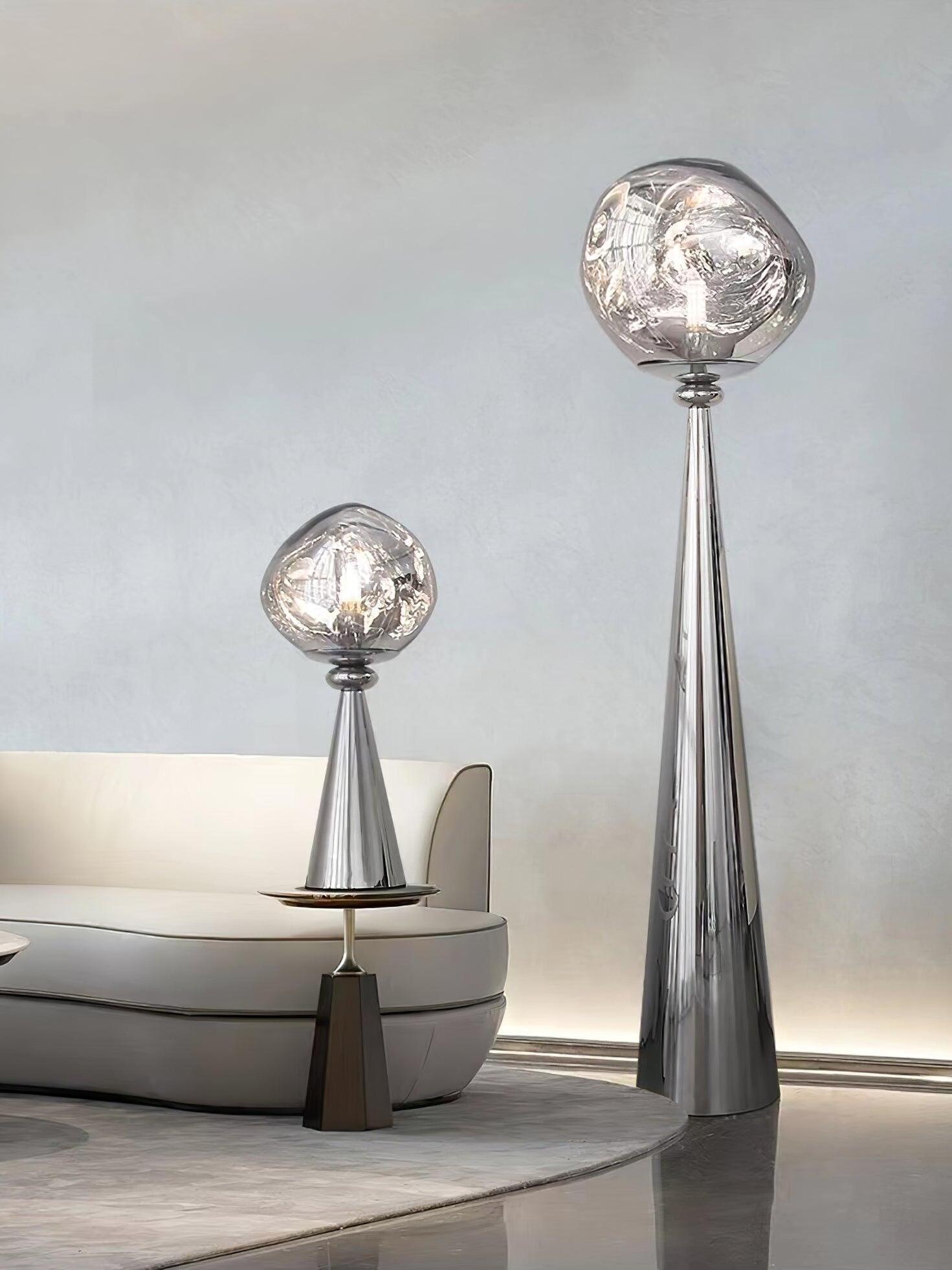 Chrome globe table lamp on a side table beside a gray sofa and a tall matching floor lamp