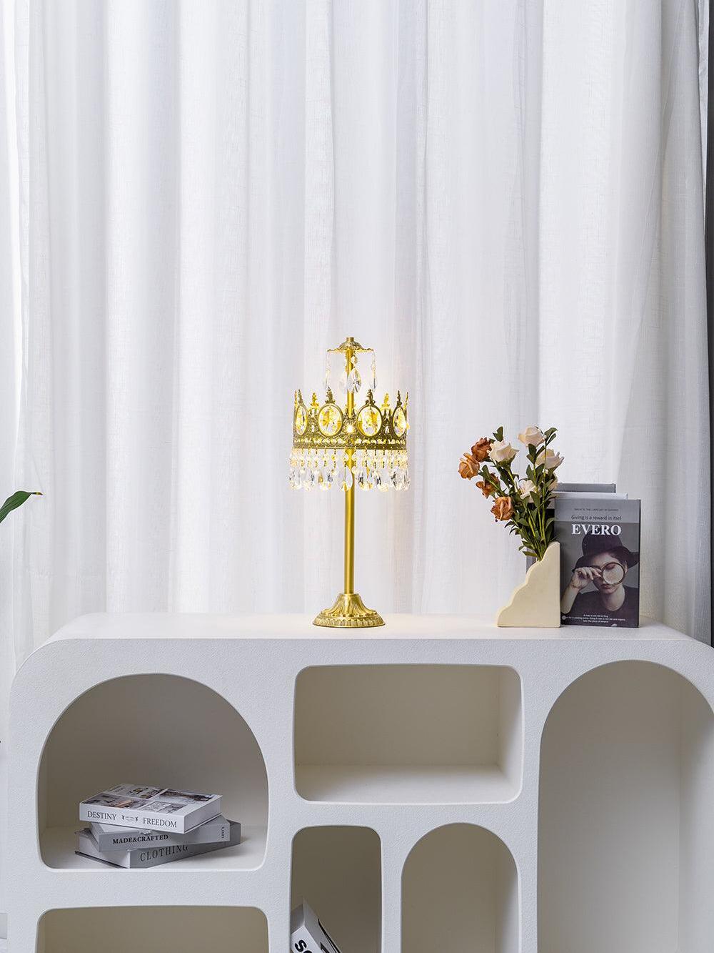 Wide view of a crystal table lamp on an arched white console with flowers and a book.