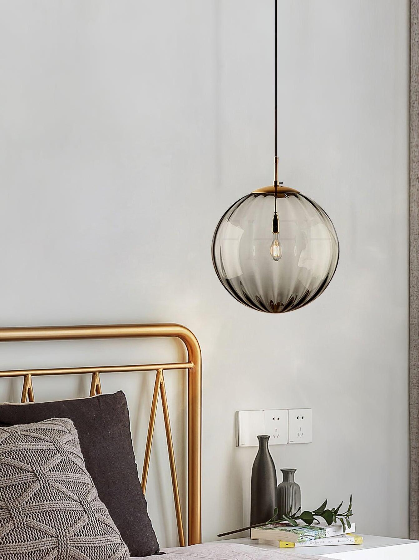 Smoke gray glass globe pendant beside a gold-toned metal bed frame