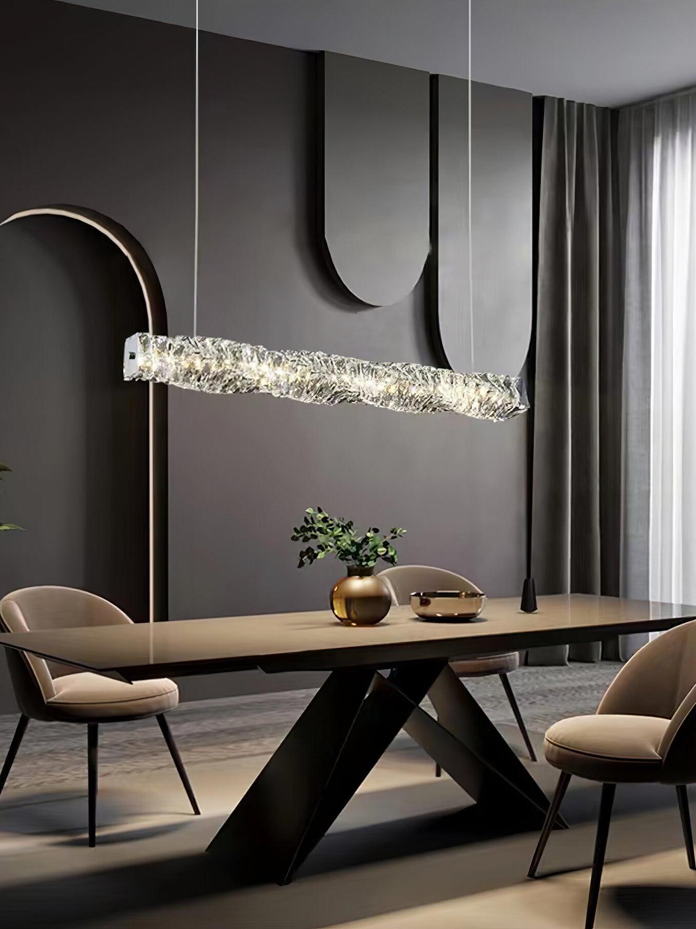 Crystal pendant above a dark dining table with V-shaped legs and curved wall decoration