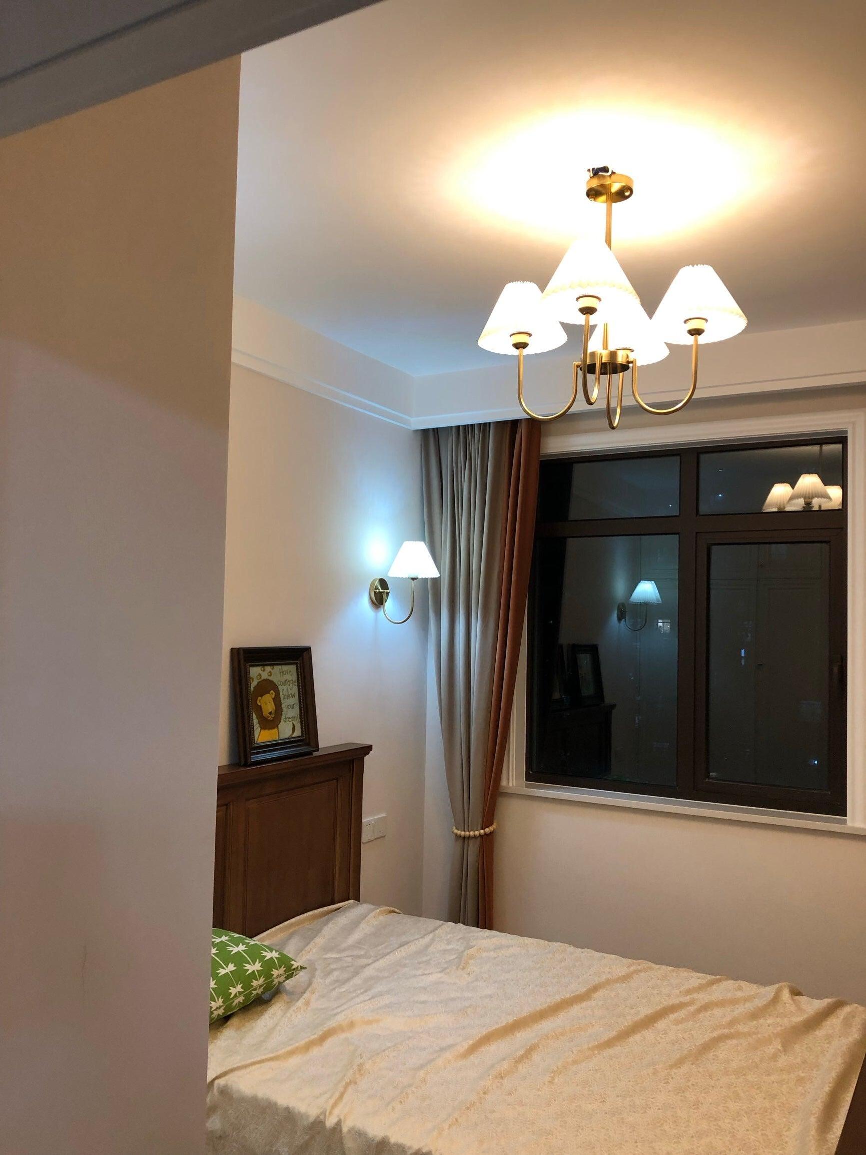 Lit chandelier above a bed beside a dark window and brown curtains