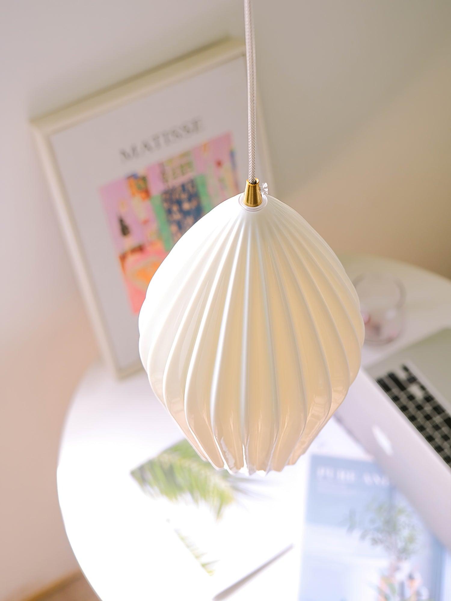 White ribbed pendant shade hanging in front of a framed print and magazines