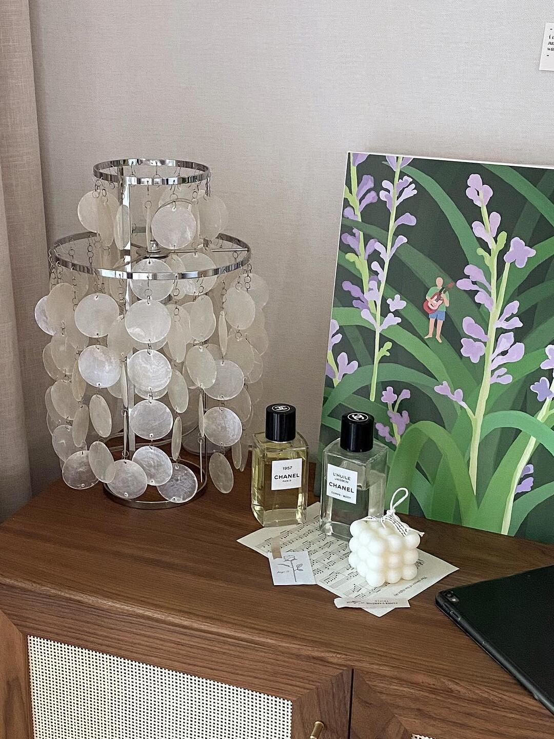 Shell lamp on wood cabinet beside perfume bottles and art