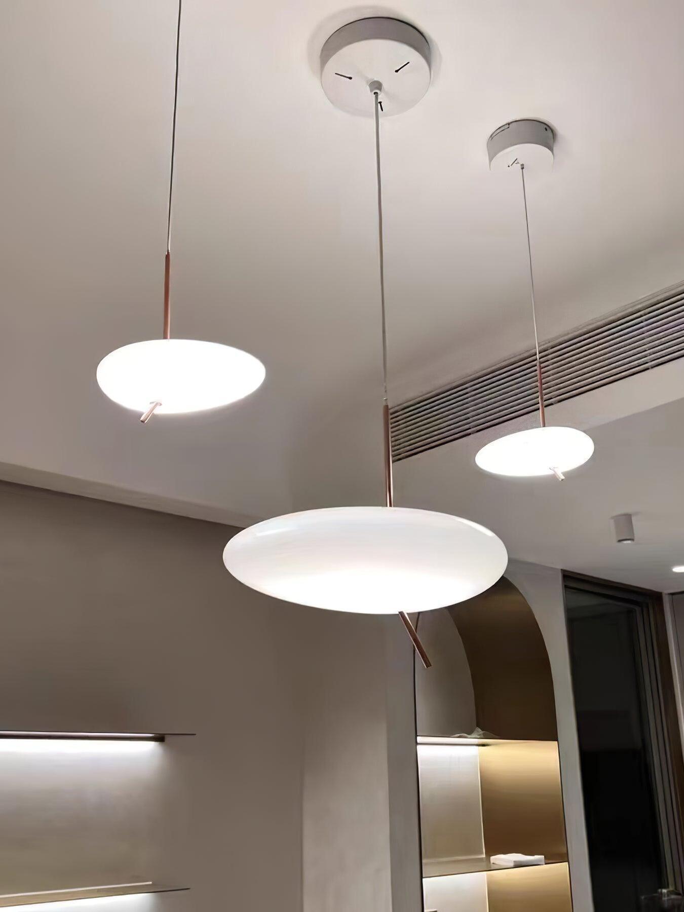 Low-angle view of three white pendant shades and separate round ceiling canopies