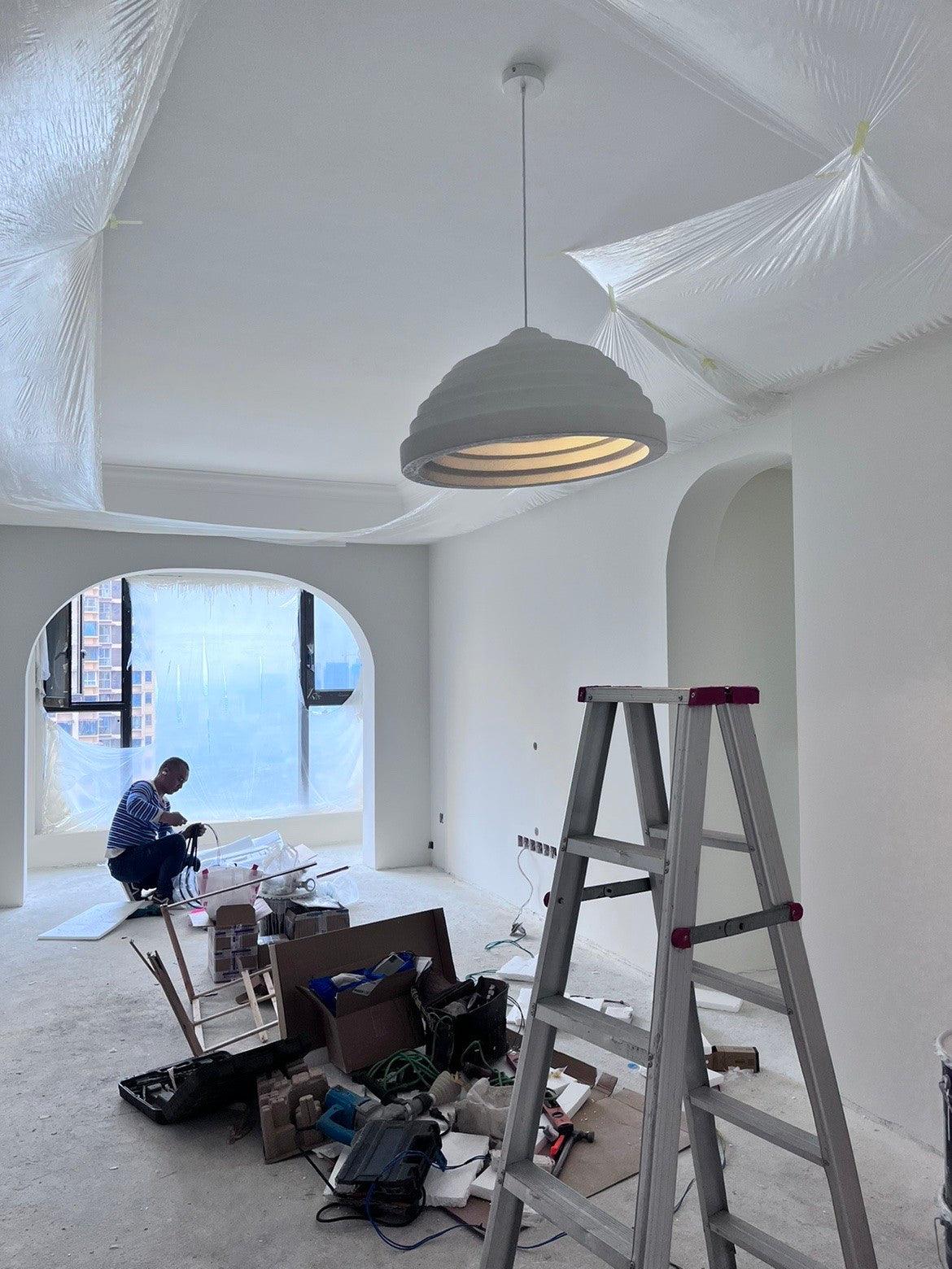 White stepped pendant in a room with a ladder, tools and a person working near a window.