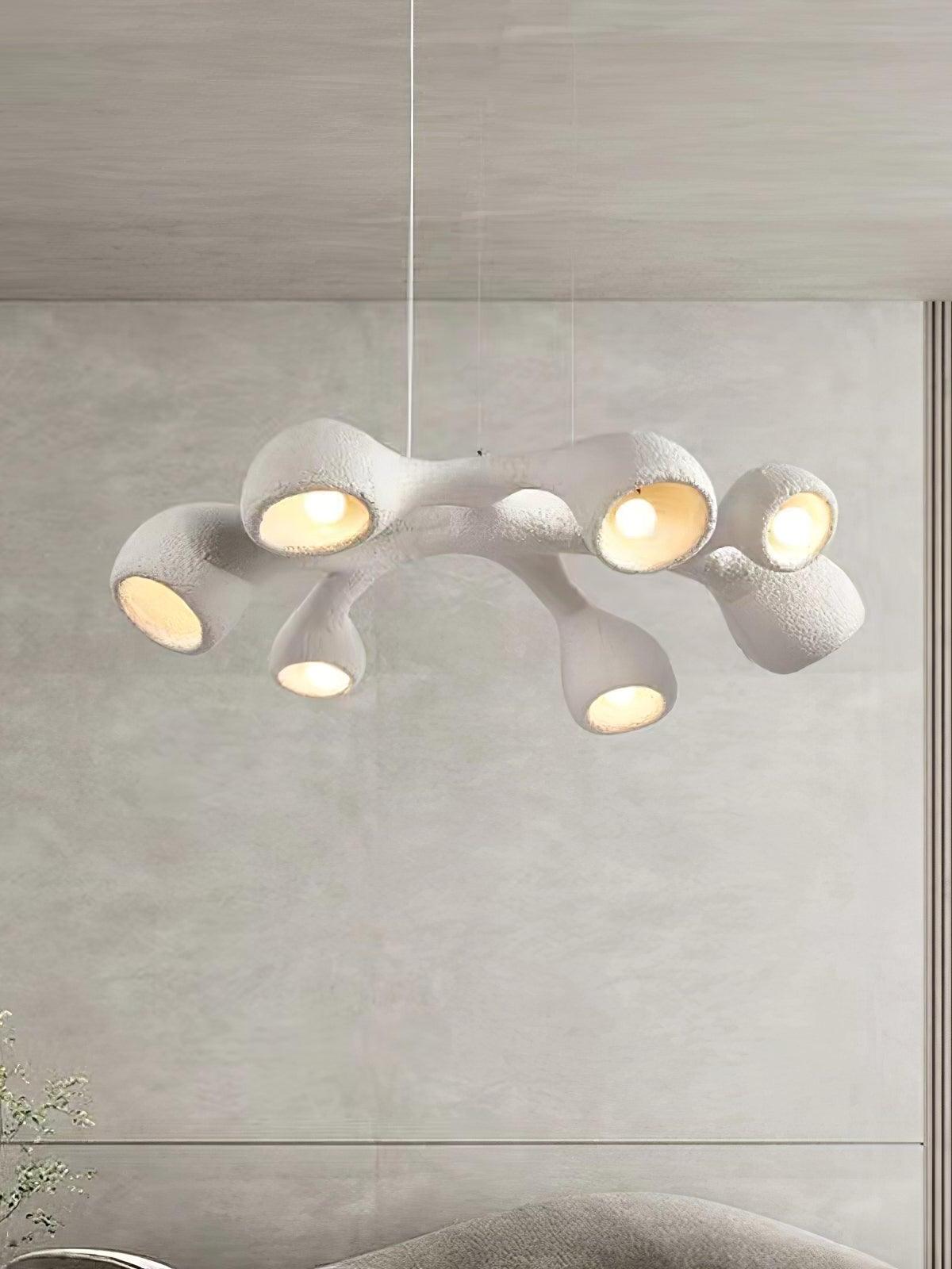 Closer room view of the white looped branching pendant with glowing bulbs before a pale wall panel