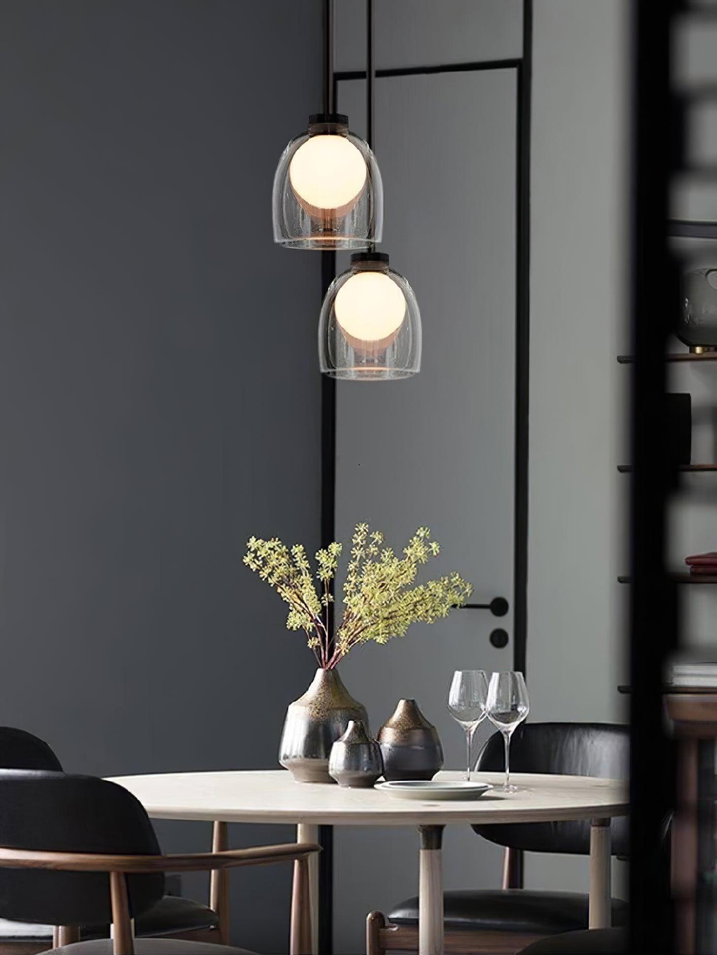Two illuminated clear Crux pendants above a table with yellow branches and glassware