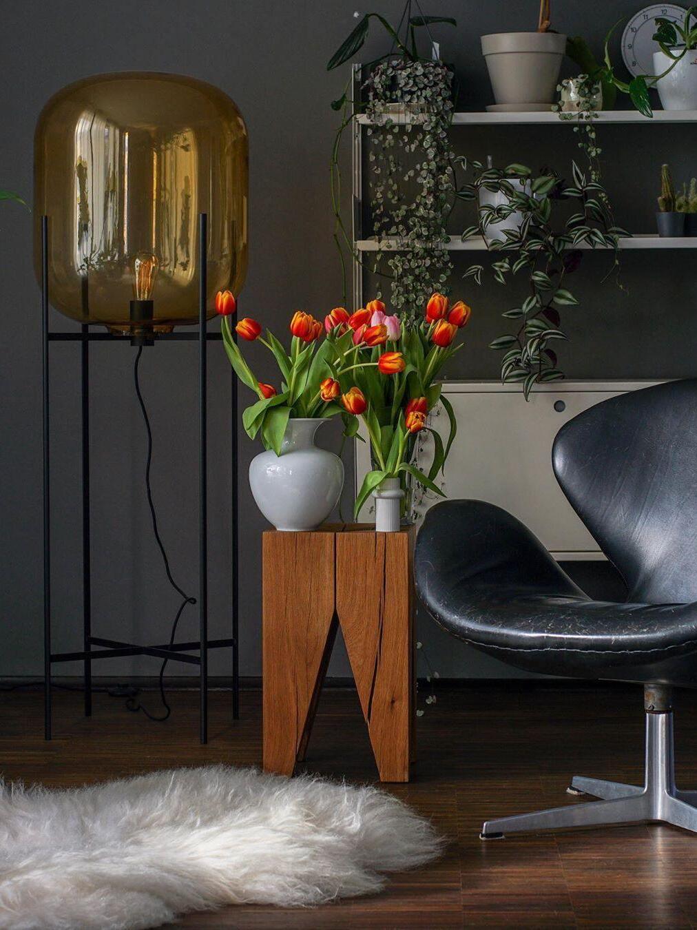 Amber-tinted floor lamp near red tulips and a black lounge chair.