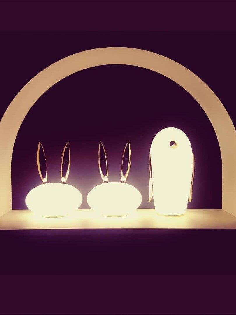 Two glowing rabbit lamps and one penguin inside arch with purple background
