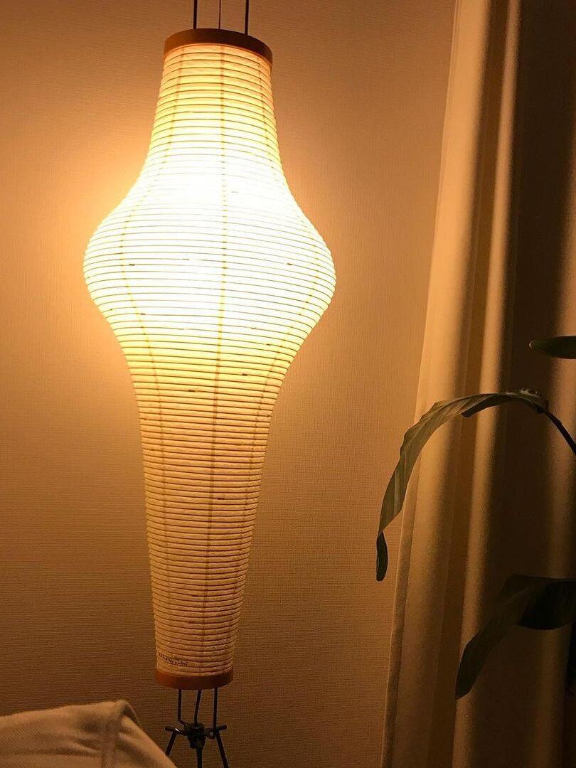 Tall paper lamp illuminated warm beside a wall