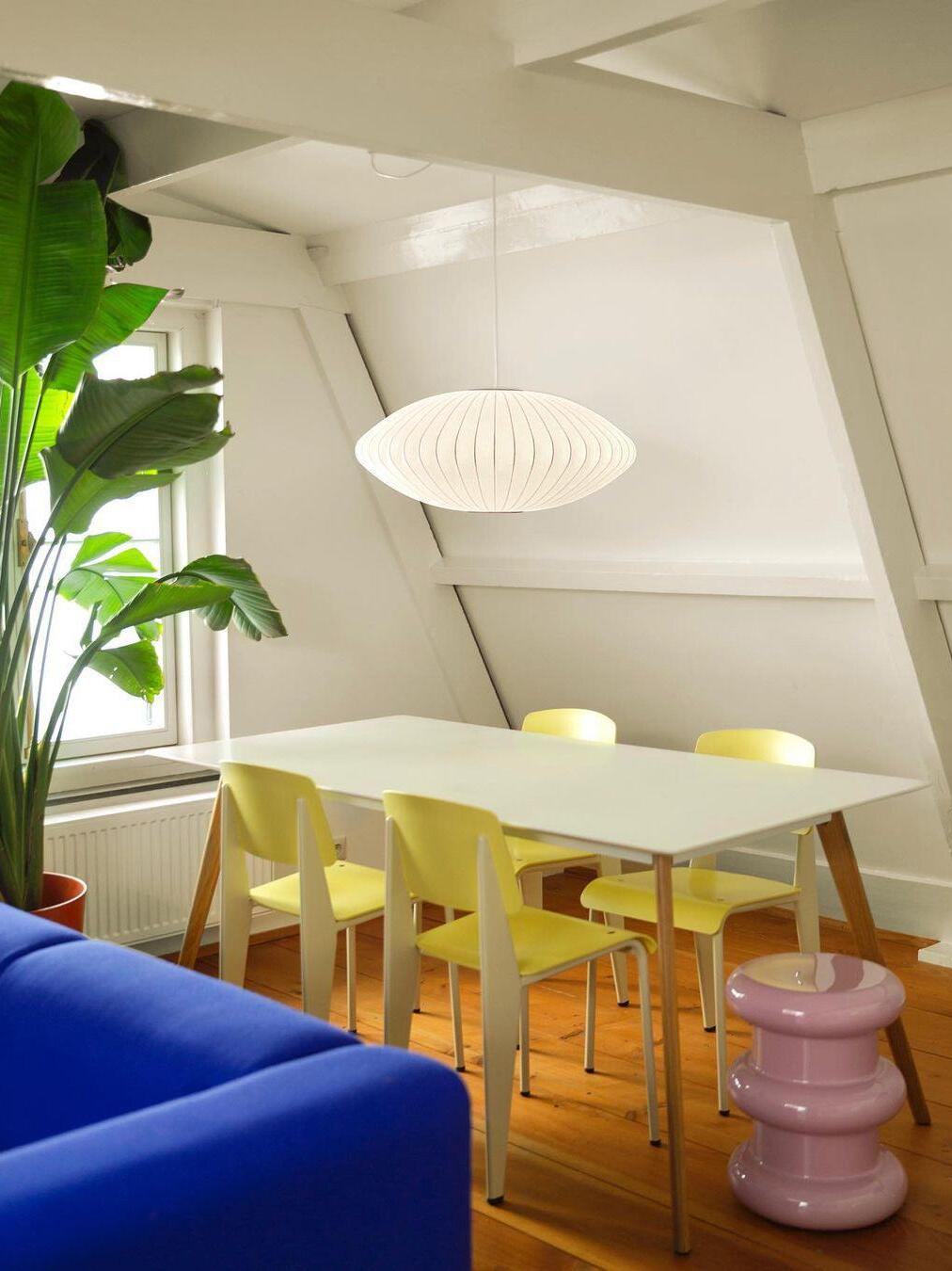 Glowing oval ribbed pendant above a pale table and yellow chairs in a sloped-ceiling room