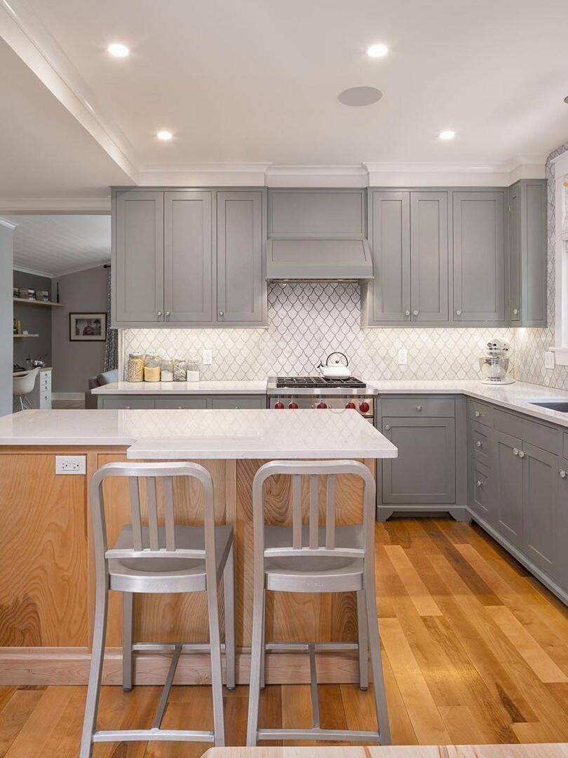 Grey kitchen with white island, two stools and recessed ceiling lights