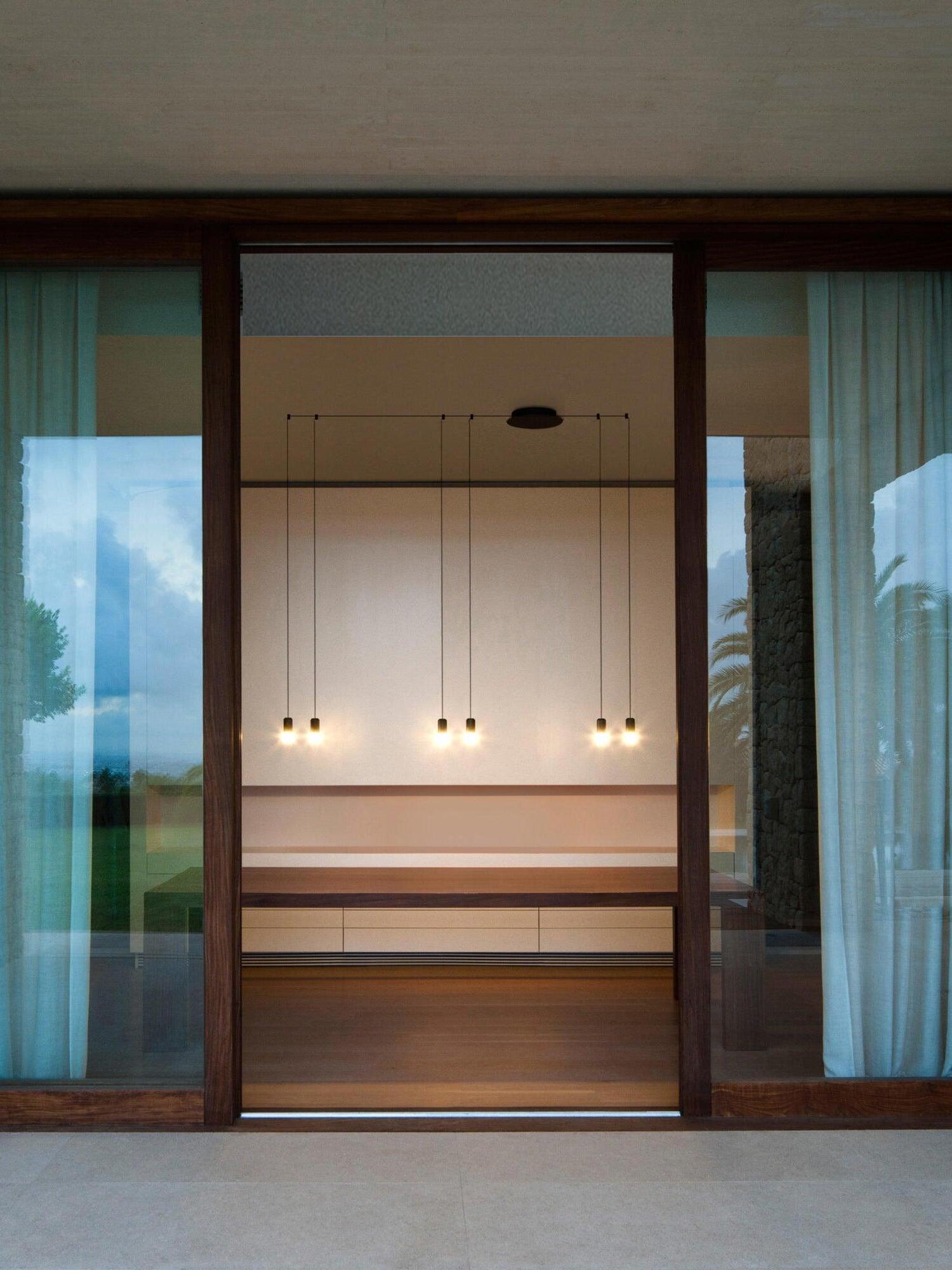 Six lit pendant heads seen through a doorway framed by wood and blue curtains