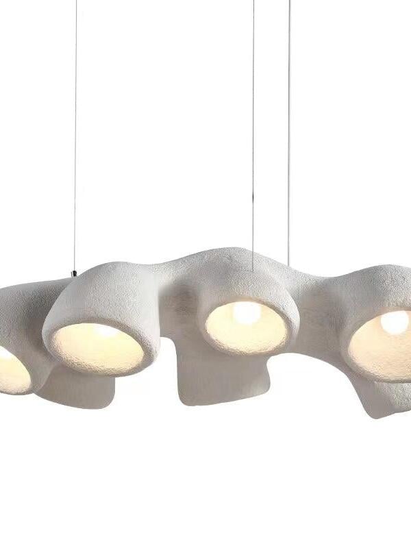 Close view of an elongated white undulating pendant with bell-like outlets, visible bulb and thin wires