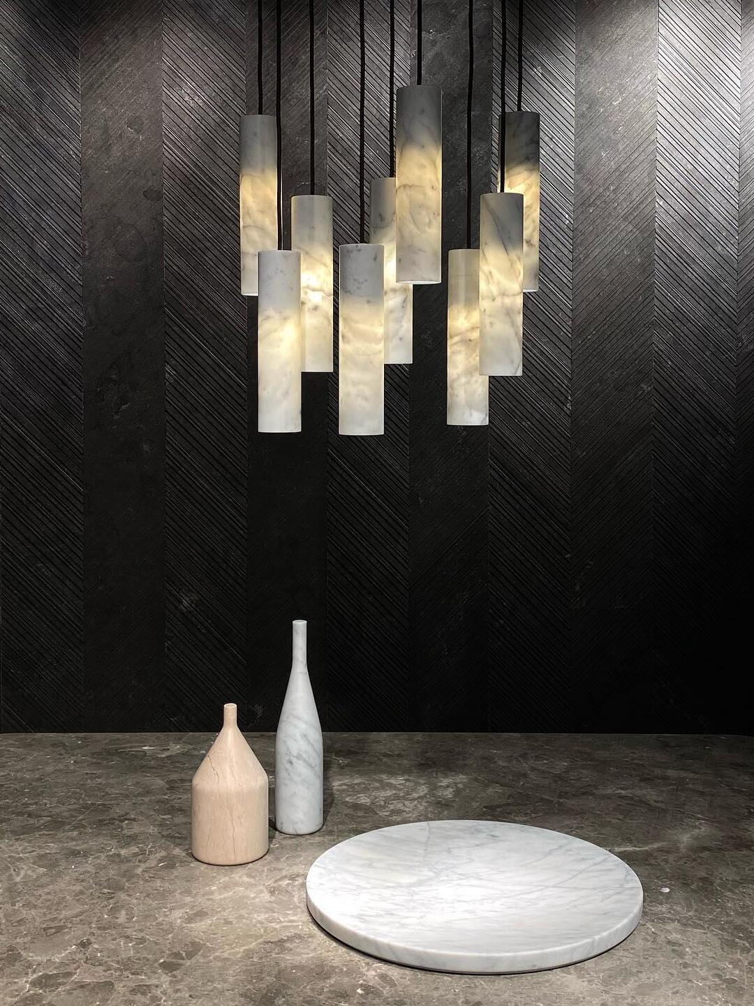 Glowing Silo cylinder pendants at varied heights above a stone tabletop with two vases and a plate