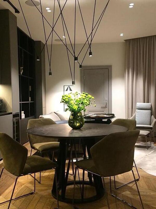 Black angular suspended lights above a round dining table with a vase of flowers and upholstered chairs