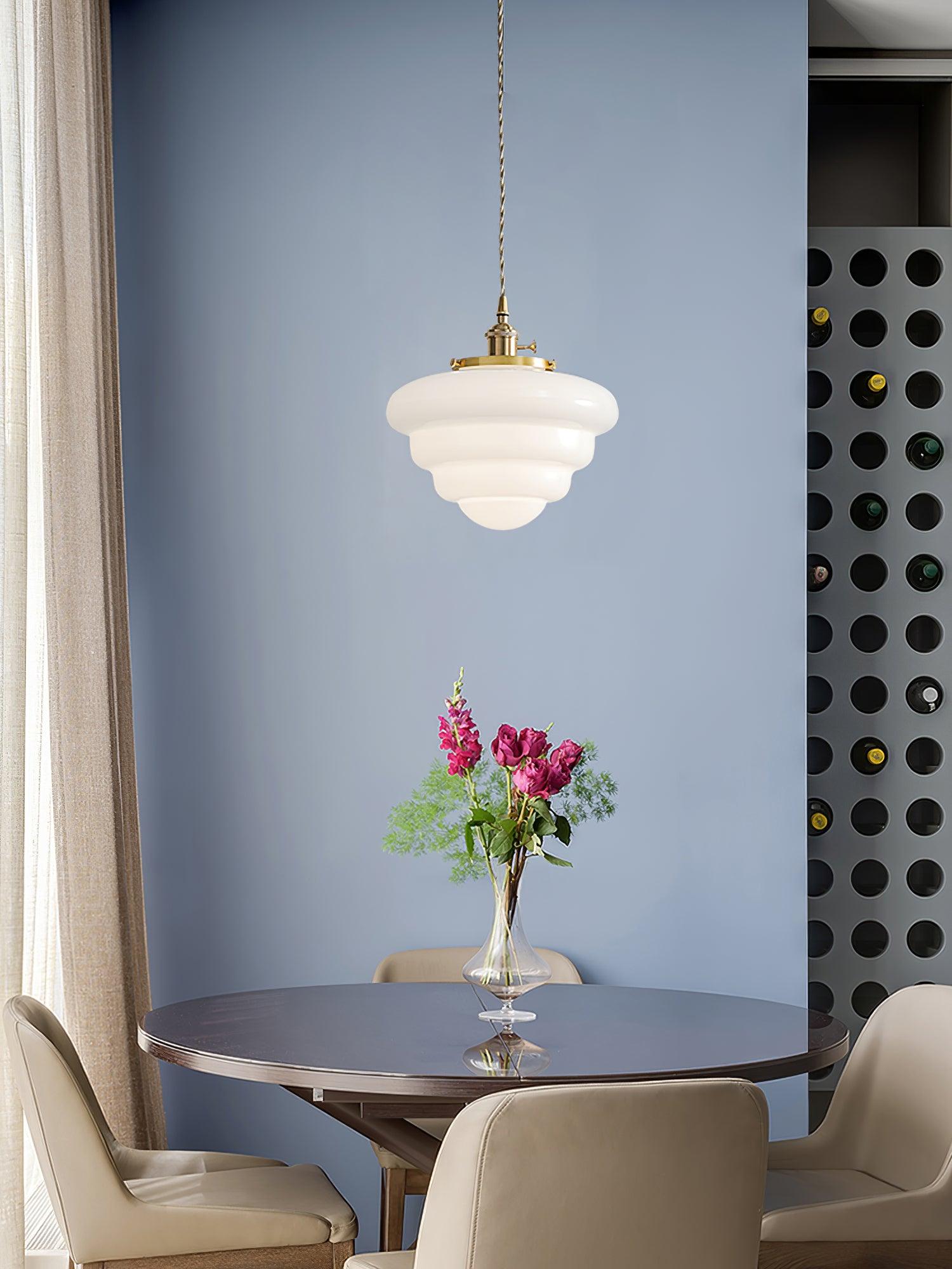 Single lit Atlas Model B pendant above a dark round table with pink flowers, beige chairs and a blue wall