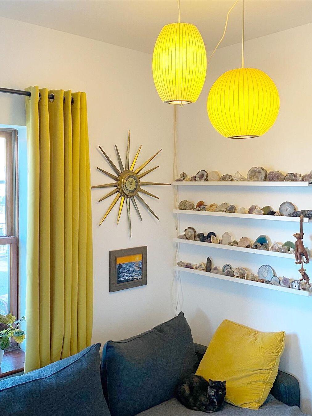 Two glowing ribbed pendants, one tall and one round, above a sofa and display shelves