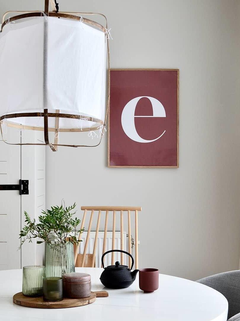 White fabric sleeve tied to bamboo frame over round dining table with teapot, cup, green vases and red letter artwork