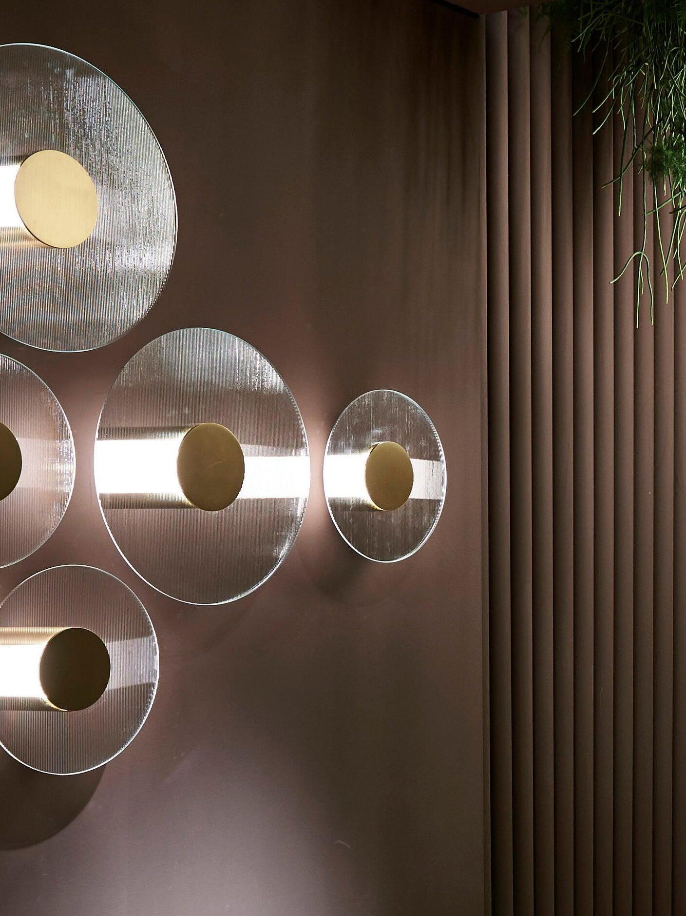 Round ribbed-glass Button wall lights with gold-coloured centres beside vertical wall ribs and trailing foliage