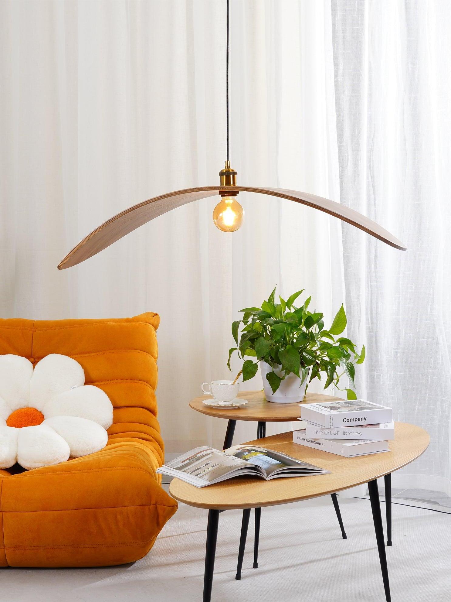 Light wood-tone curved pendant above an oval coffee table beside an orange chair and white curtains
