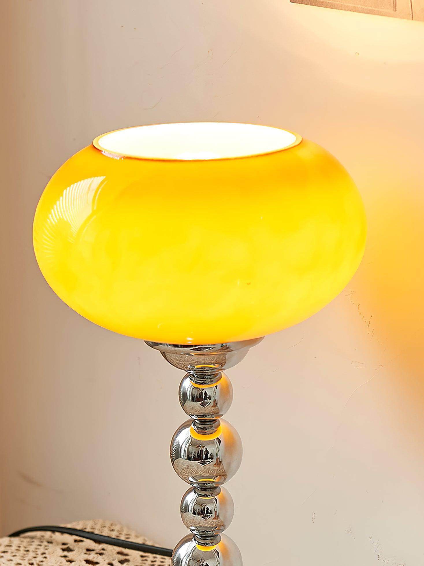 Close-up of the lit orange oval glass shade with an open upper rim and the upper rounded chrome stem