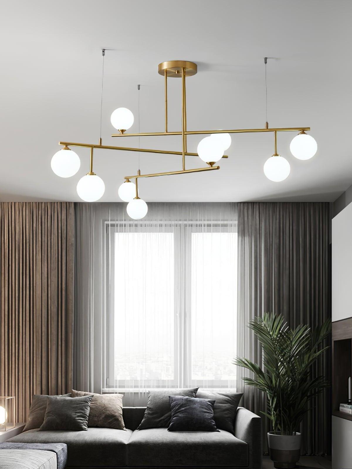 Brass-tone Arteriors chandelier with glowing white globes in a living room with dark curtains and a window